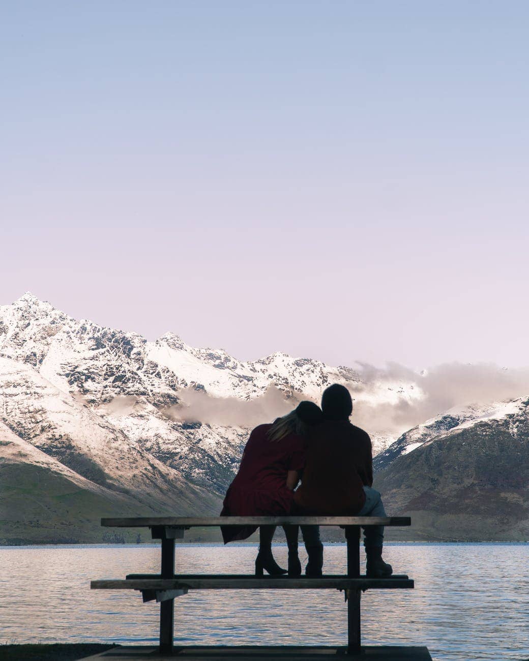 romantic couple sitting on bench and admiring lake and mountains
